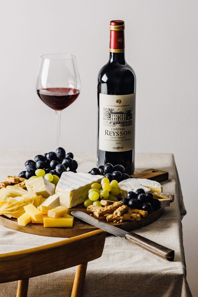 Dieses Bild zeigt ein schön angerichtetes Cheeseboard. Im Hintergrund steht eine Rotweinflasche und ein Weinglas.