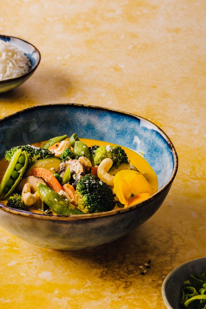 Dieses Bild zeigt ein Curry mit knackigem Gemüse und Reis, welches in blauen Schüsseln angerichtet wurde.