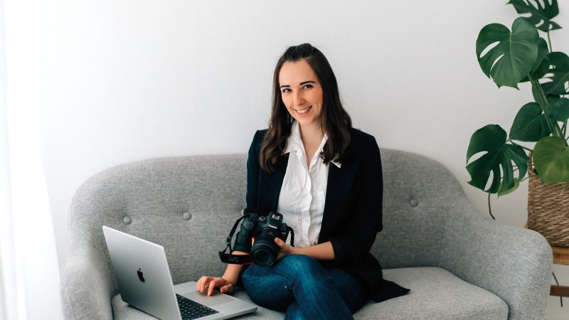 Dieses Bild zeigt die österreichische Food Fotografin Stefanie Pölzl-Huemer, welche auf einer Bank mit ihrem Laptop und ihrer Kamera sitzt.