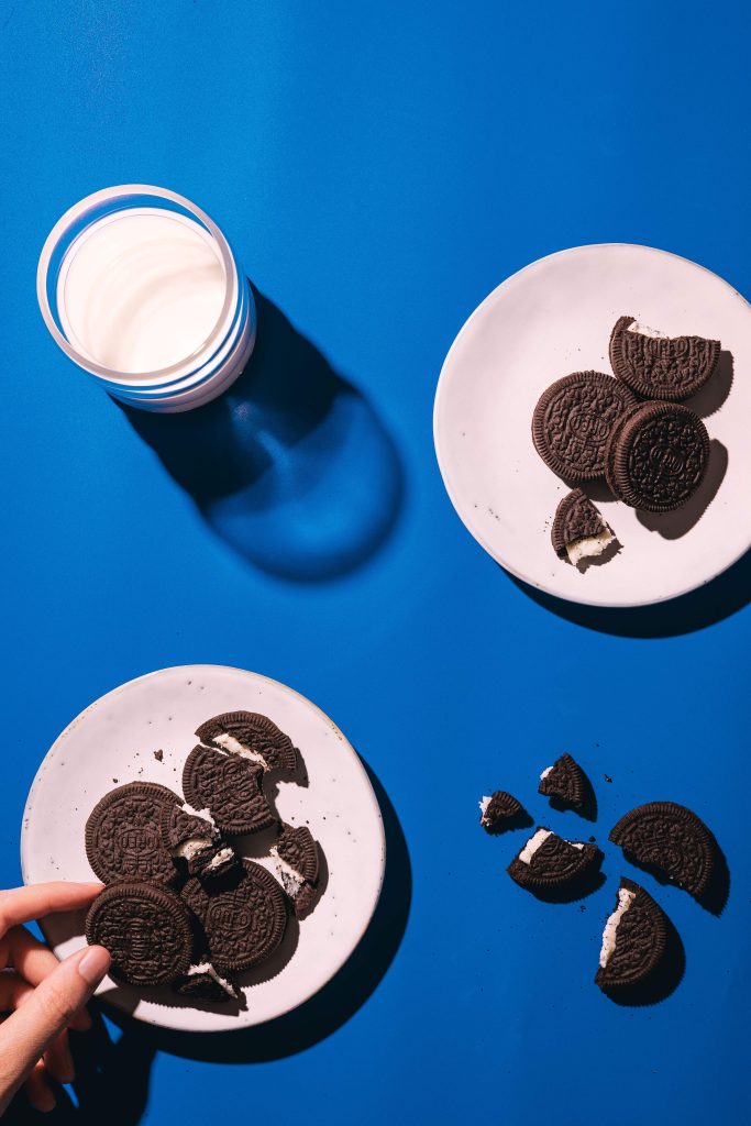 Dieses Bild zeigt ein Bild der österreichischen Food Fotografin Stefanie Pölzl-Huemer im bright and bold Stil. Darauf zu sehen ist ein blauer, einfärbiger Untergrund, Oreo Kekse und ein Glas Milch. Dabei wurde auf direktes Licht und harte Schatten gesetzt.